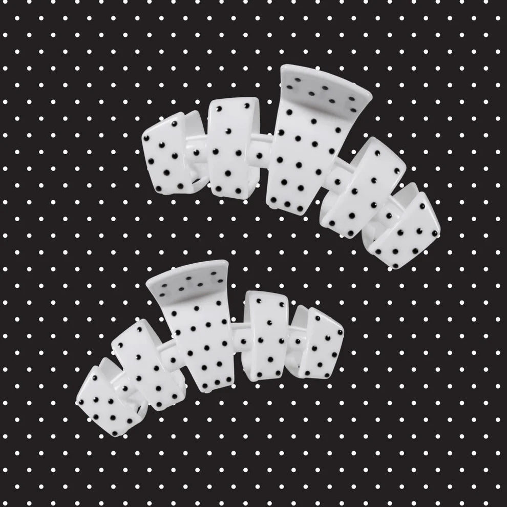 Two white plastic claw-style hair clips with black polka dots, arranged on a black background with a white polka-dot pattern.